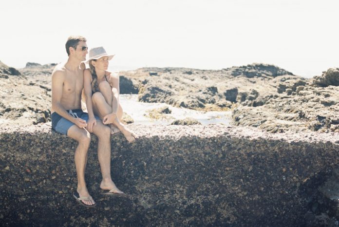 Laguna Beach,USA,A man and woman, couple on the beach sitting on a wall by a rock pool.